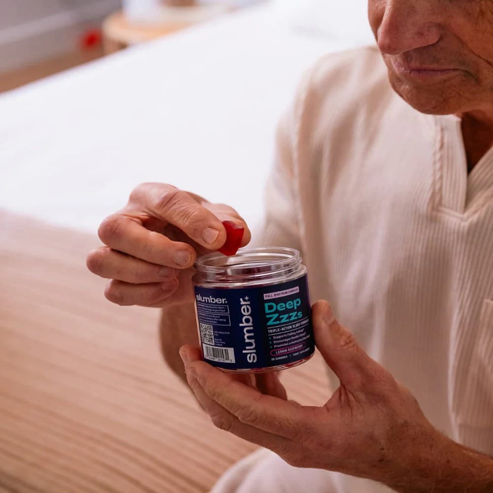 A man taking a raspberry-red Deep Zzzs gummy from the jar at bedtime